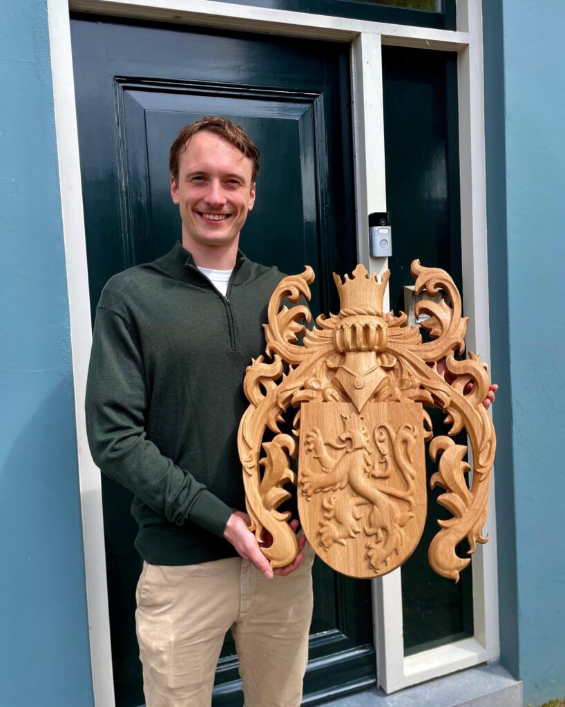 Woodcarver with finished hand-carved wooden heraldic coat of arms sculpture